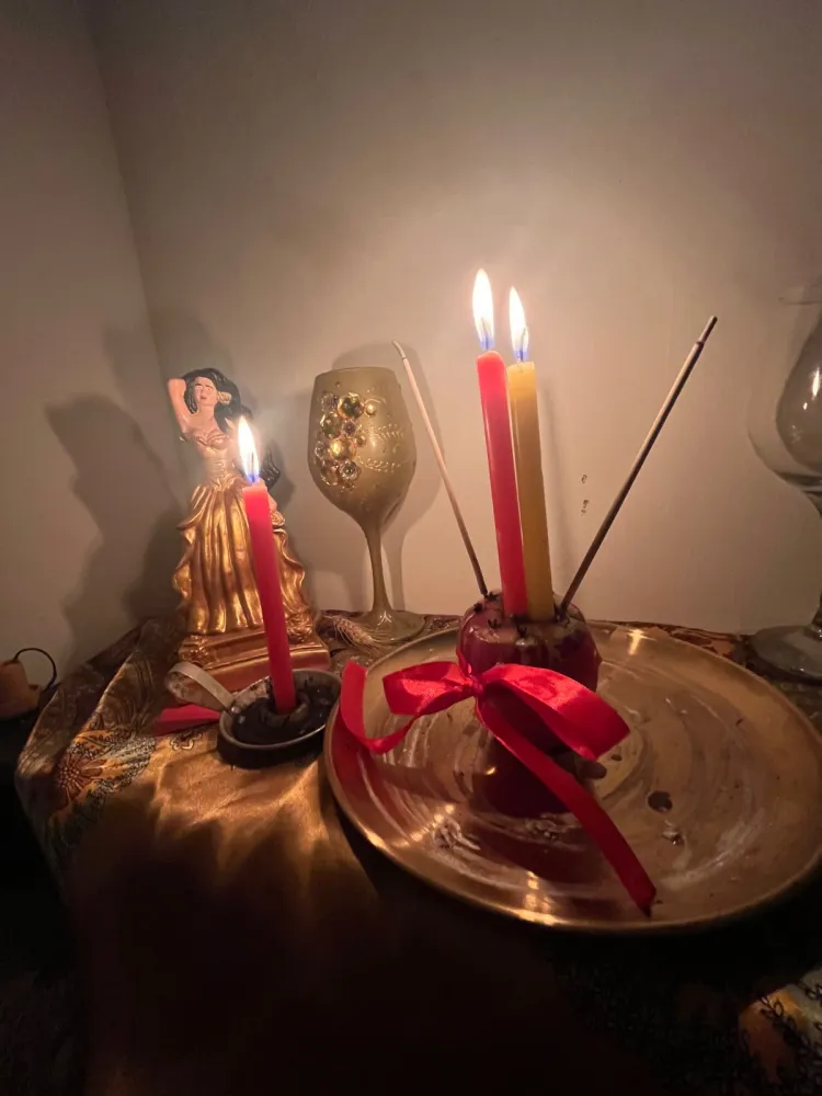 Altar com imagem de cigana dourada, taça, velas vermelha e amarela acesas e maçã amarrada com fita vermelha