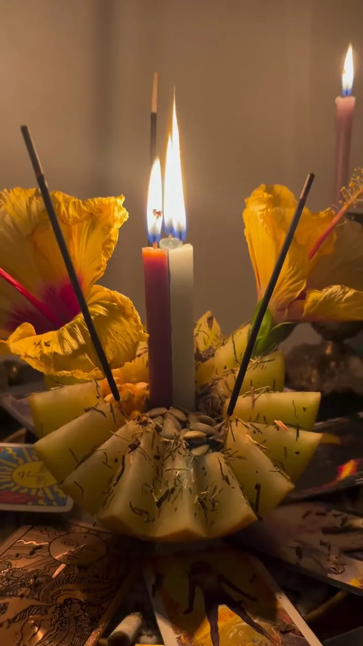 Oferenda com hibiscos amarelos, velas e incensos sobre cartas de tarot