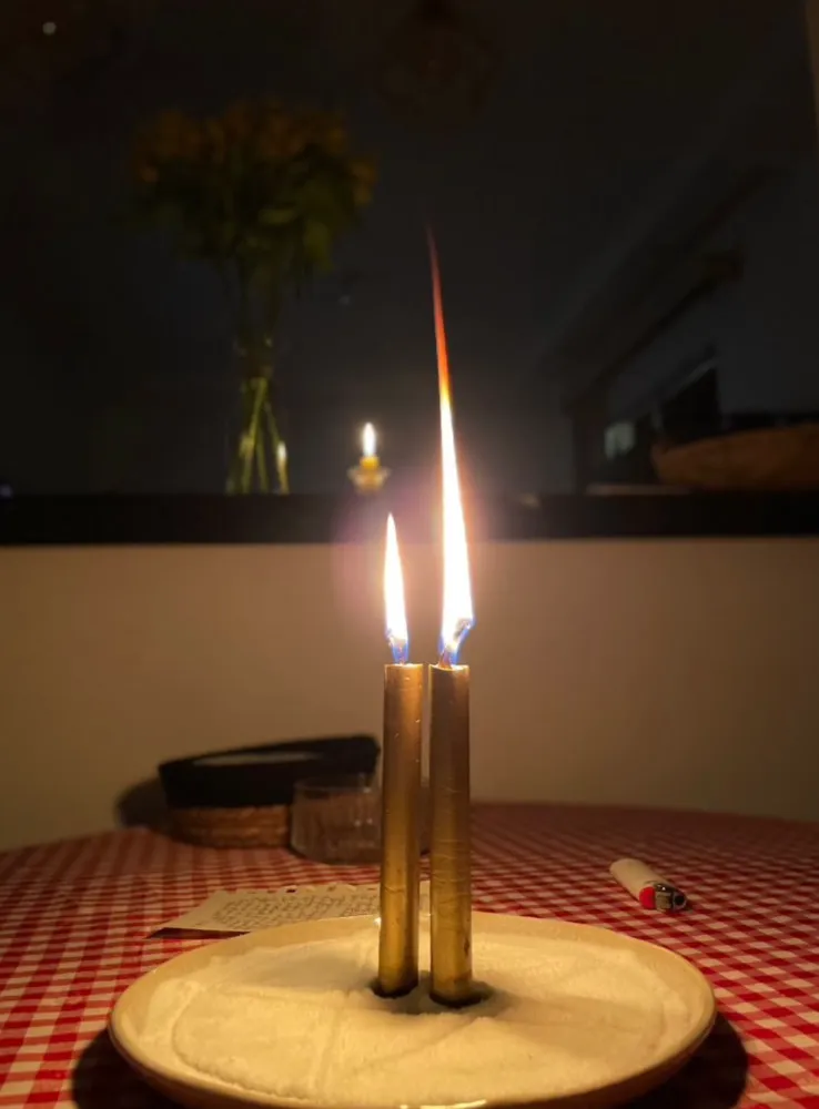 Duas velas douradas acesas sobre prato com açúcar e um pedido escrito em papel